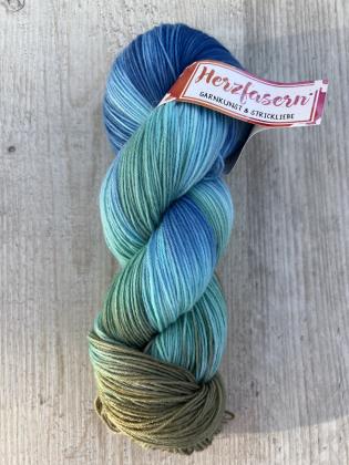 ALT-Text Hauptbild: Handgefärbter Strang Herzfasern No. 20 in Blau-, Türkis- und Grüntönen, Farbe Fjordküste, liegend auf hellem Holz